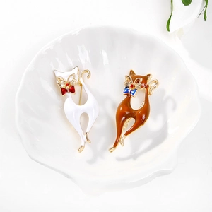 Détail de broches chat en émail blanc et caramel avec nœuds sur un plateau blanc