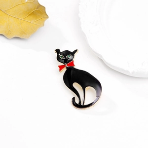 Broche chat en émail noir avec nœud rouge et yeux en pierres précieuses vertes sur fond blanc