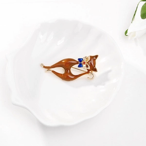 Broche chat rétro marron ambre avec nœud bleu présentée dans un plateau blanc