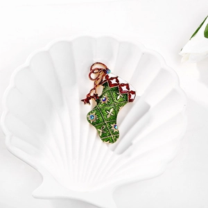 Detail of green Christmas stocking brooch with enamel finish and blue crystals on white tray