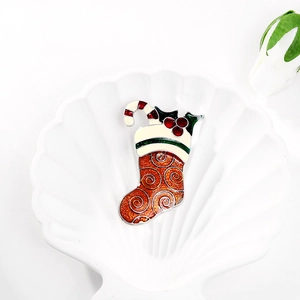 Detail view of a glittery red Christmas sock brooch with holly leaves on a white tray