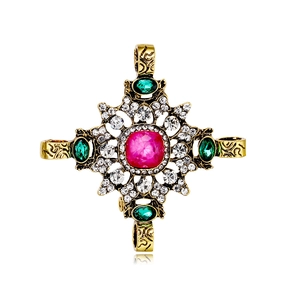 Broche croix baroque avec pierre centrale rose et accents émeraude sur métal doré