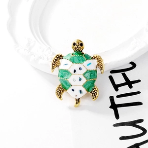 Detailed top view of a gold-toned turtle brooch with green enamel and metal textures