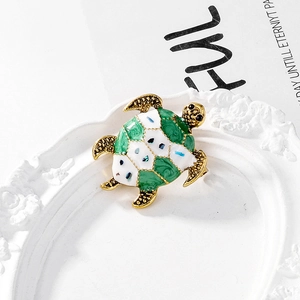 Macro detail of golden sea turtle brooch with green and white enamel on a vintage tray
