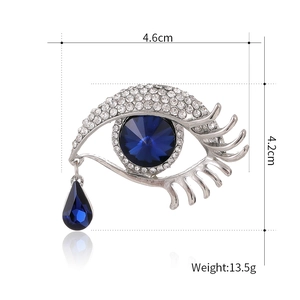 Broche œil argentée avec pupille en cristal bleu et pendentif goutte sur blanc