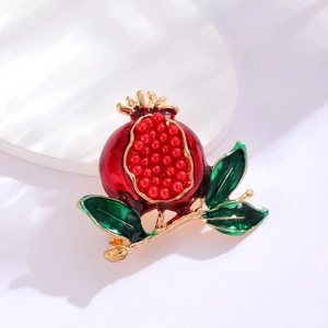 Macro shot of pomegranate brooch with red enamel and beaded seeds on a white background