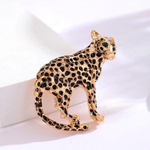 Broche léopard vintage dorée avec émail noir et yeux en pierres vertes sur fond blanc