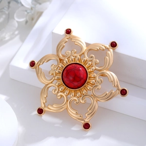 Détail d'une broche lotus vintage avec finition dorée mate et incrustation de pierres rouges