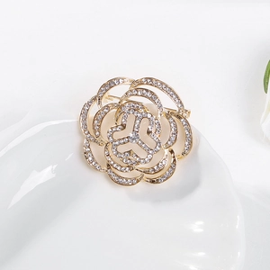 Gros plan d'une broche camélia en métal doré sertie de cristaux brillants sur céramique blanche