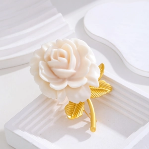 Elegant cream rose brooch with gold-tone leaves on a minimalist tiered display stand