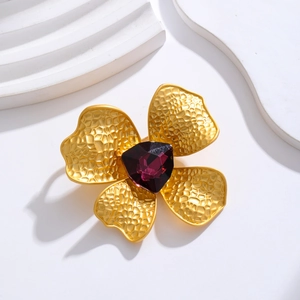 Detail of matte gold flower brooch featuring hammered petals and a large purple crystal stone