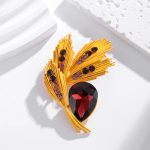 Macro detail of golden wheat brooch with red teardrop gemstone and purple rhinestones