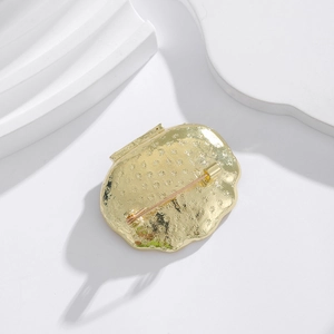 Elegant gold shell brooch featuring detailed snowflake pattern and secure safety pin fastener
