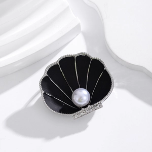 Detailed close-up of shell-shaped brooch with black enamel, crystals and center pearl