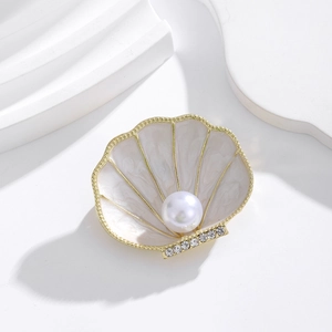 Close-up of shell-shaped brooch with white pearl, gold plating and sparkling crystals