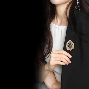 Detailed view of a vintage peacock brooch with green gemstone on a black blazer jacket