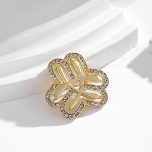 Detail of gold hollow flower brooch with white rhinestones on minimalist white stand