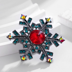 Vintage snowflake brooch with red centerpiece and peacock green rhinestones on white stands