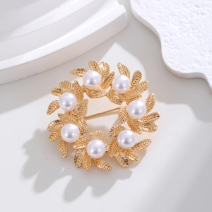 Detailed view of matte gold wreath brooch with textured leaves and seven white pearls