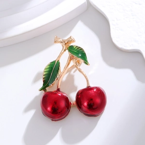 Stereo cherry brooch with red enamel and golden leaves on a white geometric stand