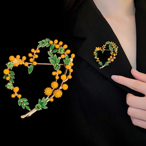 Detail of a vintage heart brooch with yellow mimosa beads and green enamel leaves