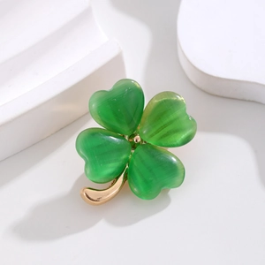 Elegante gouden klaverspeld met groene kattenoogstenen op een witte esthetische achtergrond