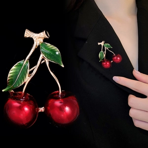 Detailed macro view and model shot of a red cherry brooch pin on a black suit jacket