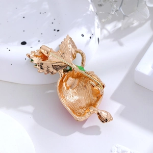 Detail view of the gold-tone metal brooch with a classic pin closure and green enamel leaf
