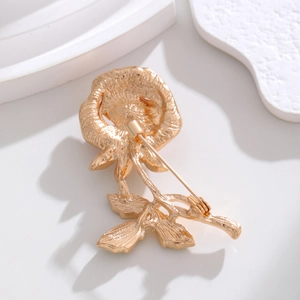 Elegant gold rose brooch with crystal details shown on a white geometric display stand