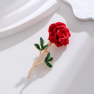 Macro detail of a red rose brooch with green enamel leaves and golden stem on white stone