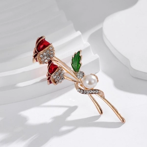 Close-up of elegant gold alloy rose brooch with red enamel buds and sparkling rhinestones