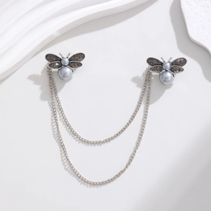Détail de la broche abeille argentée avec perles grises et chaînes sur fond blanc