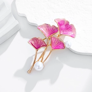 Détail macro d'une broche ginkgo dorée avec émail dégradé rose et perles