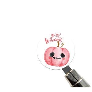Detailed macro view of pink watercolor Halloween pumpkin sticker held by metal tweezers
