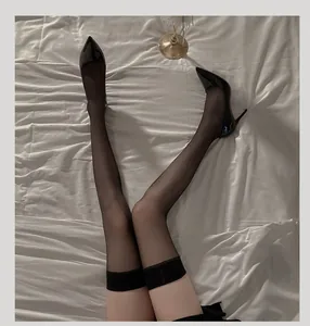 Detail of sheer black thigh high stockings with wide band and black stilettos on bed