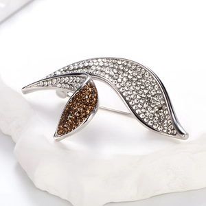 Dettaglio macro di una spilla a foglia argento con strass bianchi e ambrati a contrasto