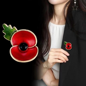 Red poppy flower brooch with green leaf and gold trim on black suit lapel backdrop