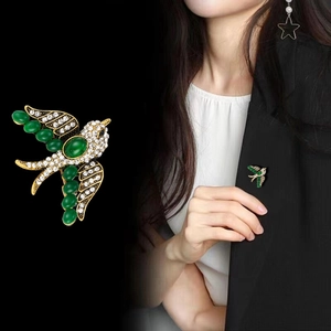Golden swift bird brooch with green gemstones and white rhinestones on black background