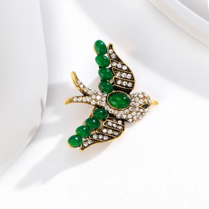Detailed view of swift bird brooch with green gemstones and white crystals on gold base