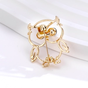Minimalist gold owl brooch featuring a hollow silhouette design on a white platform