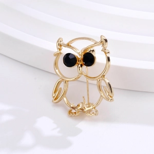 Detailed macro of golden owl brooch featuring sparkling black gemstone eyes and sleek finish