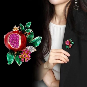 Elegant red pomegranate brooch with pink rhinestones and green leaves on black background