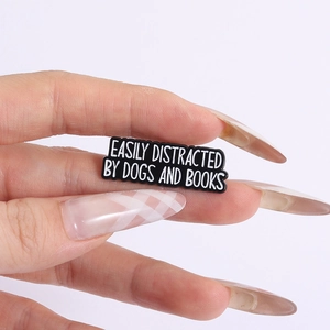 Detail of hand holding black enamel pin engraved with Easily Distracted by Dogs and Books
