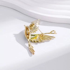Elegant gold-plated flying bird brooch showing its back secure pin and green enamel details