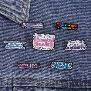Macro detail of seven colorful mental health enamel pins on dark blue denim jacket