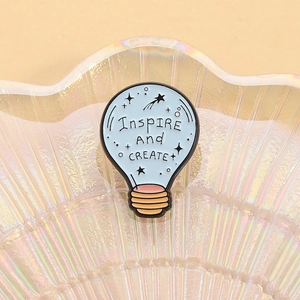 Creative light bulb enamel pin with inspire and create text on a decorative shell tray