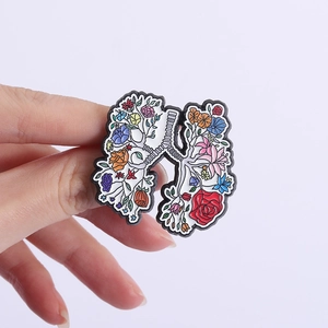 Detail of creative floral lung enamel pin badge being held by hand on grey background