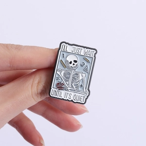 Close-up of skeleton enamel pin with 'I'll Just Wait' text and office stationery detail