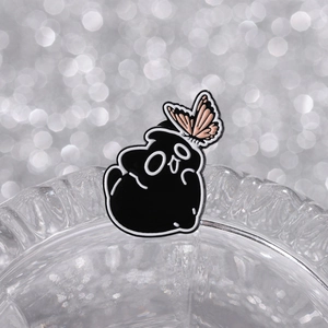 Detail of creative black monster enamel pin with a pink butterfly on glass rim