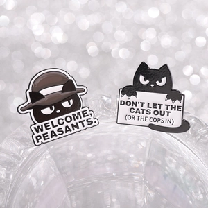 Close-up of funny black cat enamel pins featuring humorous English slogans on silver background